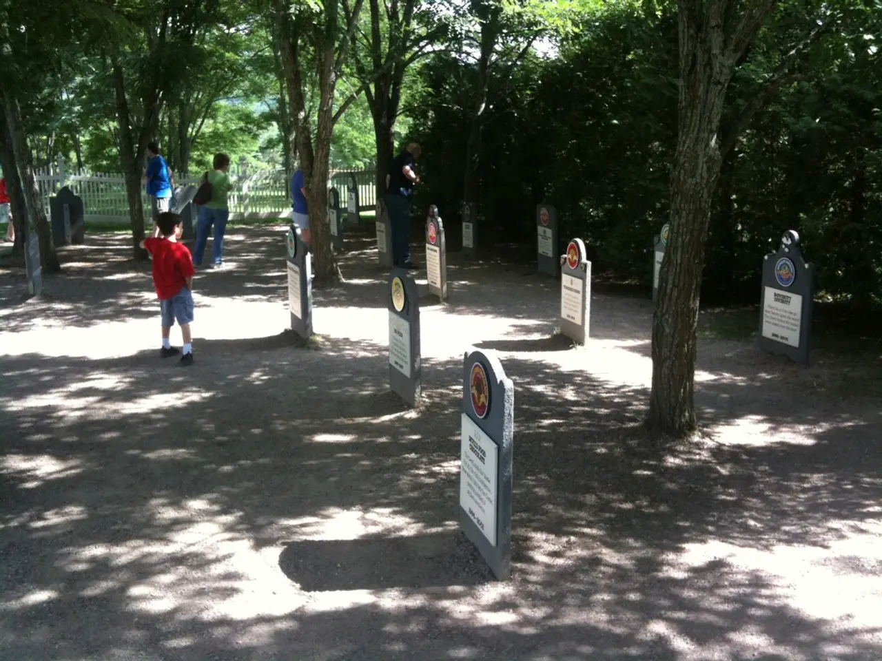 In this image there are a few people standing around in a cemetery, there are trees everywhere.