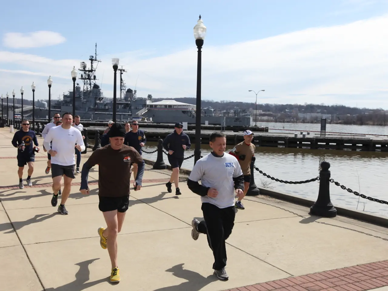 In this image there are so many people running on the bridge, beside them there are some street...