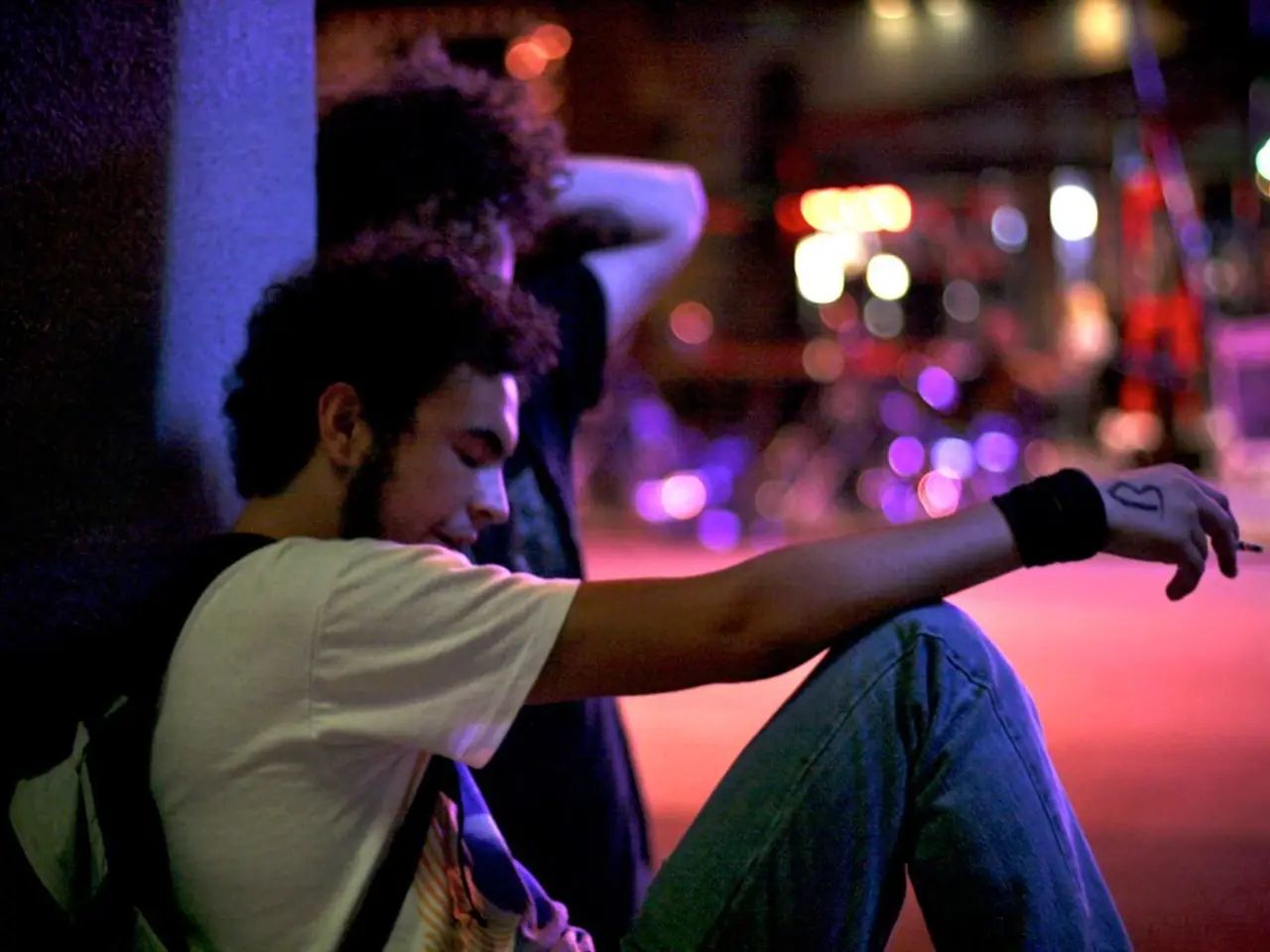 In this image we can see persons sitting on the ground and one of them is holding cigarette and bag...