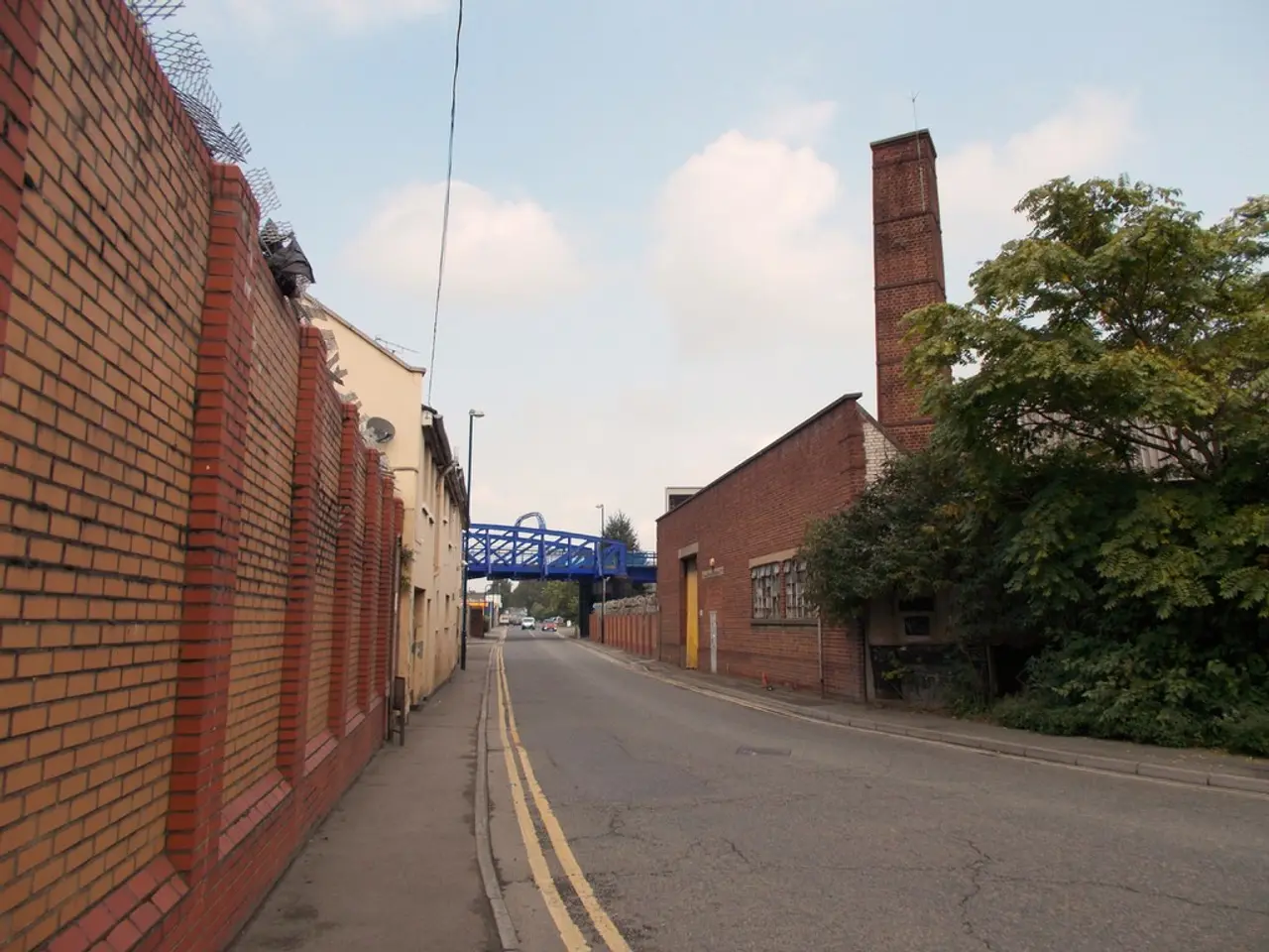 Here we can see wall,road,wire,buildings and trees. In the background we can see...