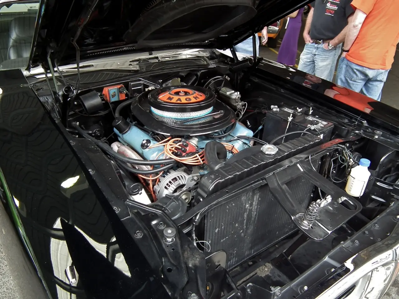 This is a zoomed in picture of a car bonnet parts. In the background of the image there are people....