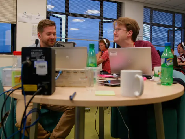 This picture shows a group of people seated and working on laptops on the table and we see a bottle...