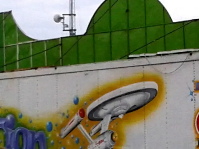 There is a car. At the back there's a wall on which painting is made.