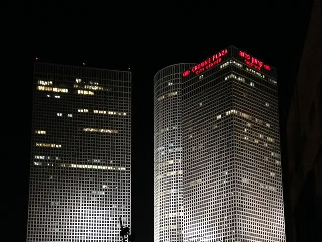 In this image there are few trees. Behind there are few buildings.