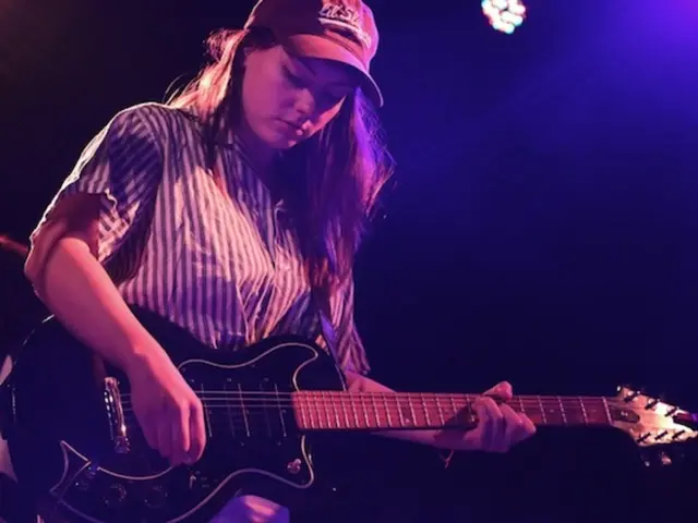 The picture is clicked in a musical concert where a lady who is wearing a cap is playing a guitar...