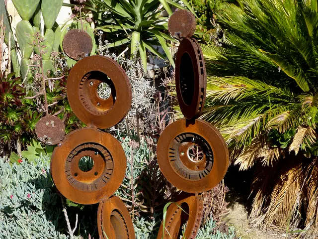 In this image there is a metal sculpture on the land having few plants, grass and trees are on it.